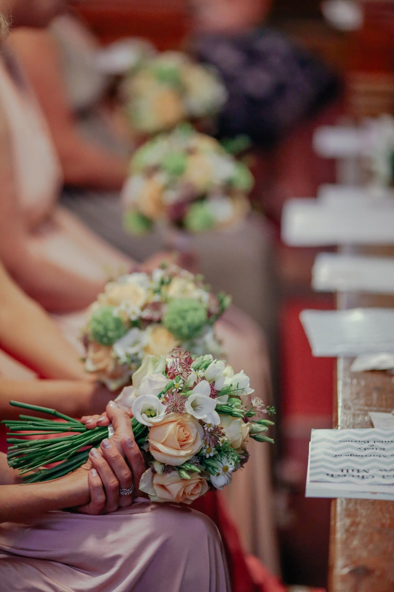 Bridesmaids seated in a church pew holding cream and peach rose bouquets