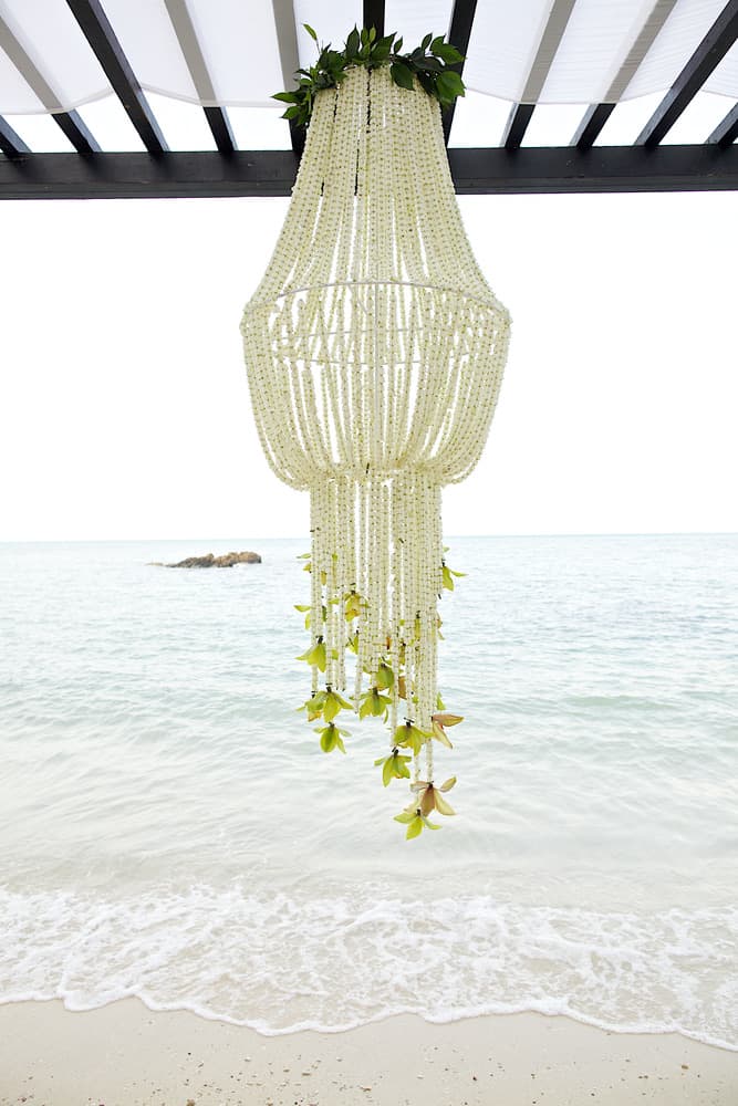 A beaded chandelier hanging above the shoreline at a beach ceremony