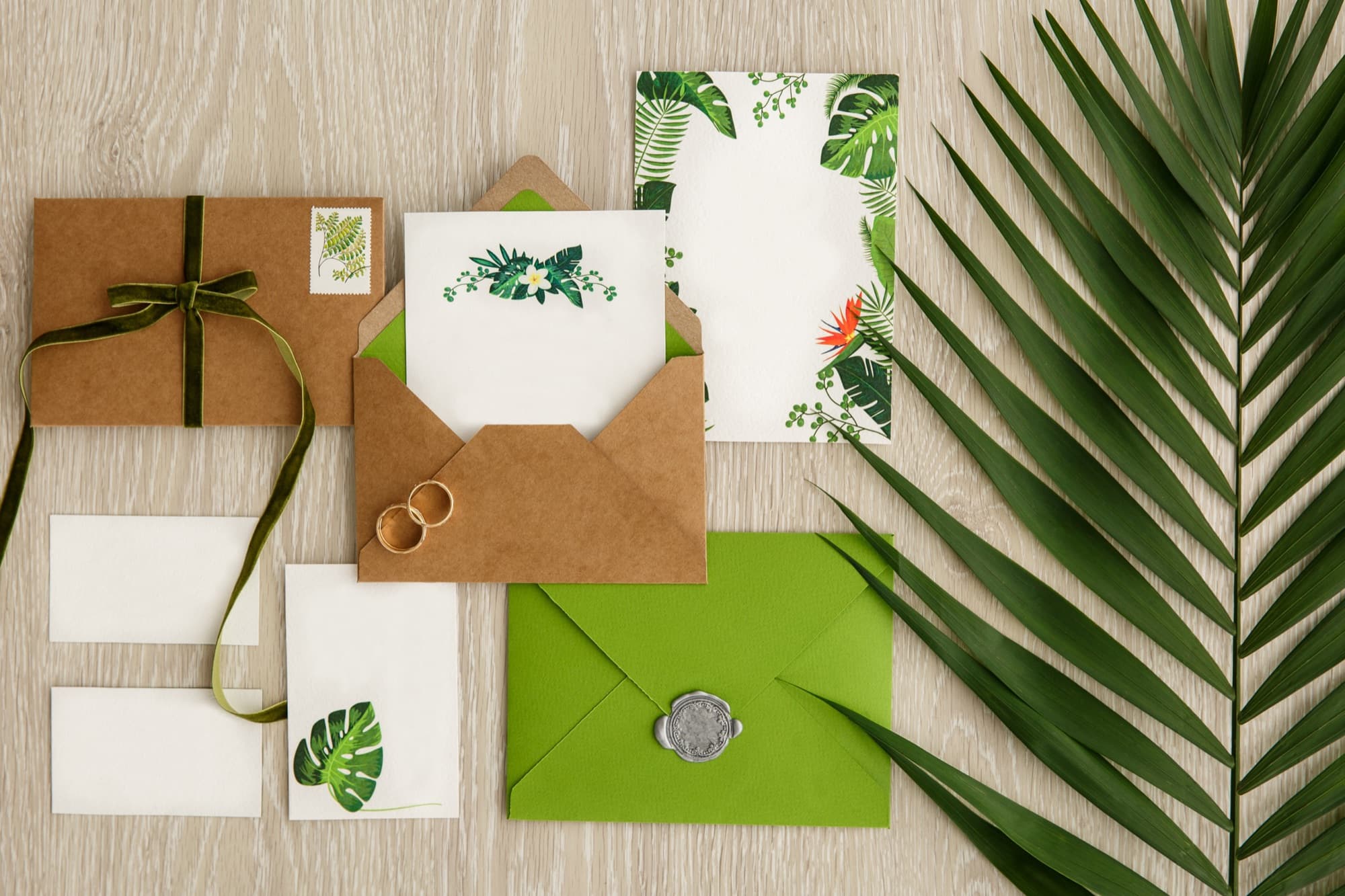 A tropical wedding stationery flat-lay with palm leaves and a wax-sealed invitation